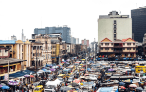 A bustling urban street market with colorful umbrellas amidst city buildings.