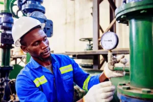 A worker in safety gear inspecting a pressure gauge in an industrial setting.