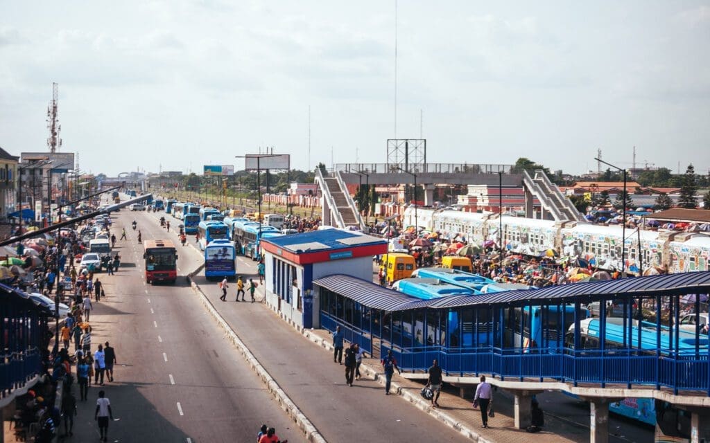 Busy urban street scene with traffic, pedestrian bridge, and crowded bus station.