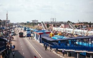 Busy urban street scene with traffic, pedestrian bridge, and crowded bus station.