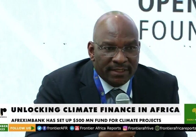 A man speaking at a conference on "unlocking climate finance in africa," with a banner indicating that afreximbank has set up a $500 million fund for climate projects.