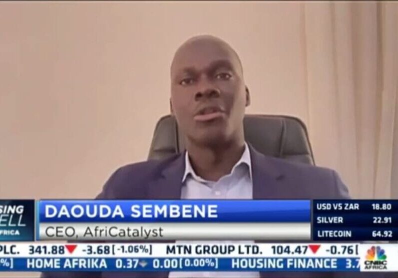 Man in business attire speaking during a television interview with financial information displayed at the bottom of the screen.