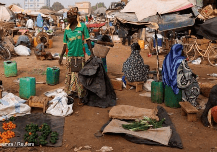 A bustling outdoor market scene with vendors and goods displayed on the ground, amid bicycles and umbrellas.