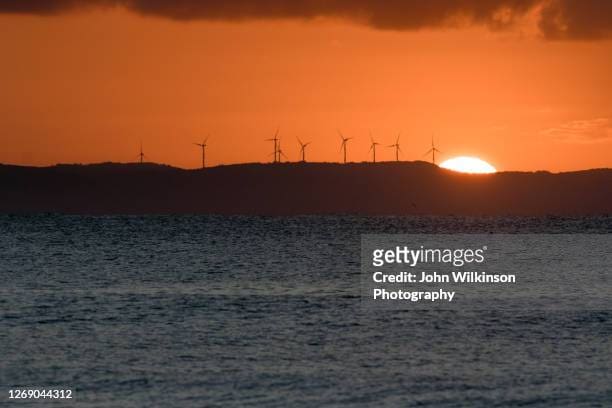 Sunset over the sea with wind turbines on the horizon.