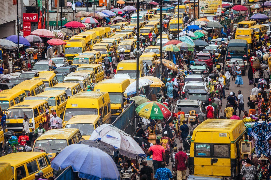 Busy street scene with heavy traffic and pedestrians amidst numerous yellow buses and colorful umbrellas.