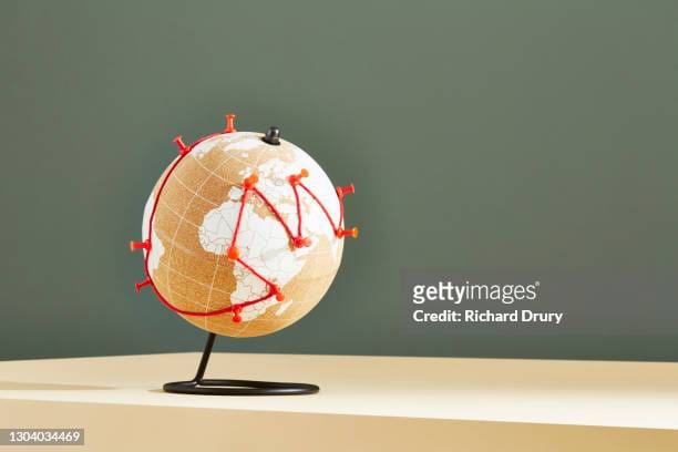 A globe with red pushpins and string creating a network of connections across continents.