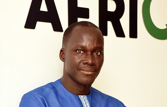 A man in a blue shirt standing in front of a sign with the word "africa.