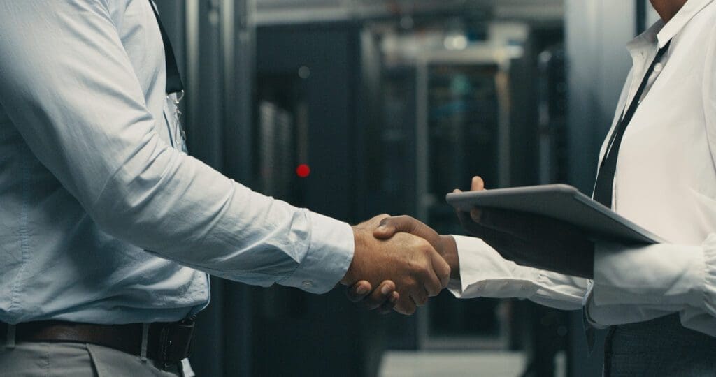 Two professionals shaking hands in a server room.