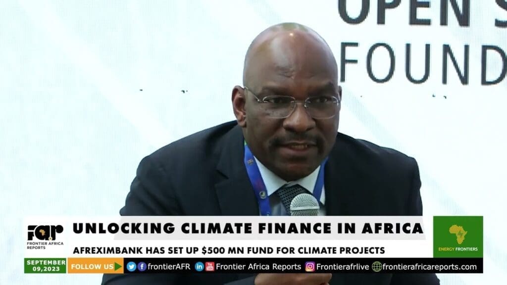 A man speaking at a conference on "unlocking climate finance in africa," with a banner indicating that afreximbank has set up a $500 million fund for climate projects.