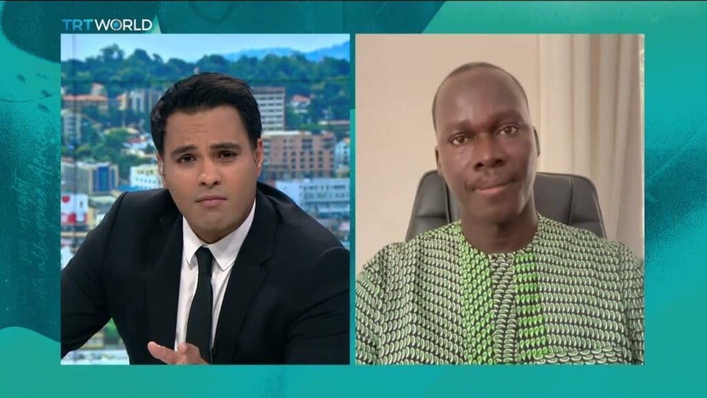 Split-screen interview with a news anchor on the left and a male guest on the right.