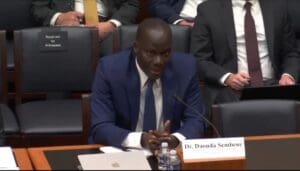 Man in a suit speaking at a hearing.