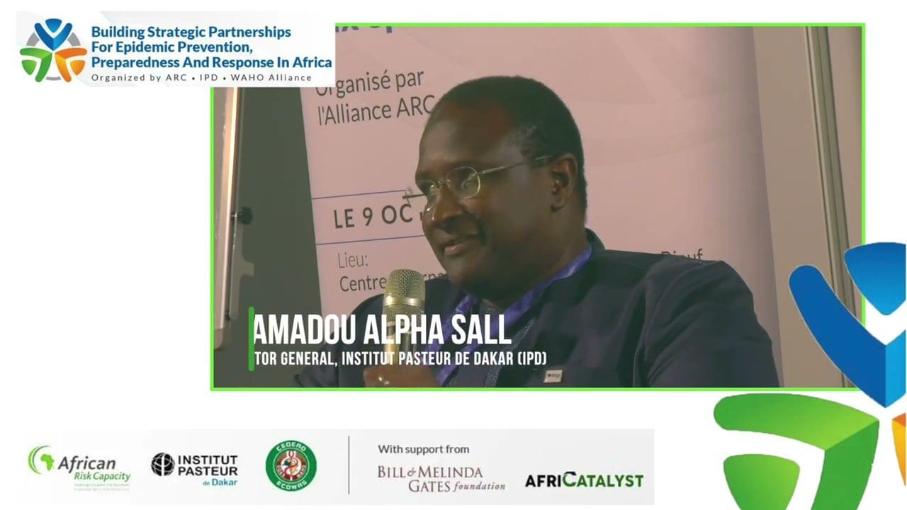A man at a conference with a name tag, "amadou alpha sall," indicating his position as the director general of the institut pasteur de dakar.