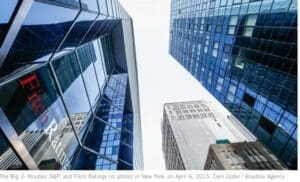Modern skyscrapers rise towards a clear sky in an urban setting, with the fitch ratings logo displayed on one building's facade.