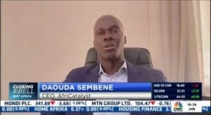 Man in business attire speaking during a television interview with financial information displayed at the bottom of the screen.