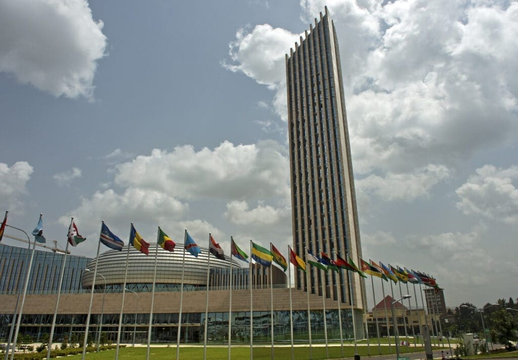 The african union headquarters building in addis ababa, ethiopia, under a partly cloudy sky, with a row of international flags displayed in front.