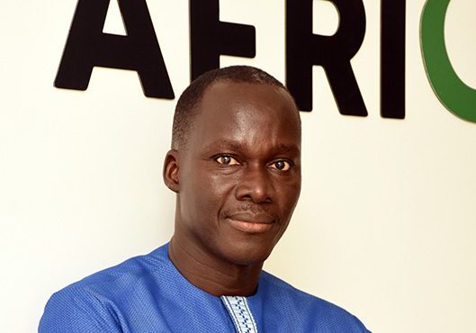 A man in a blue shirt standing in front of a sign with the word "africa.