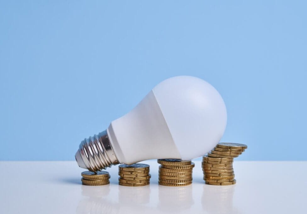 Front view of light bulb on stacked coins simulating financial growth graph. Increase in electricity bills concept.