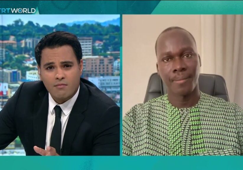 Split-screen interview with a news anchor on the left and a male guest on the right.