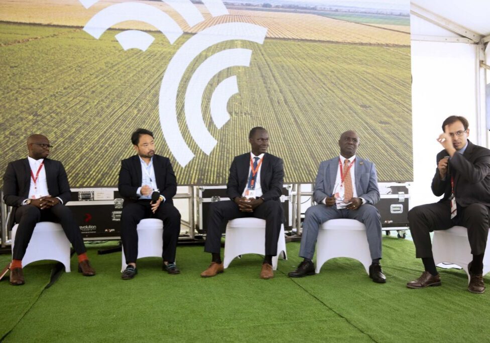 Panelists seated on stage during a conference discussion with an agricultural backdrop.