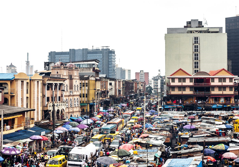 A bustling urban street market with colorful umbrellas amidst city buildings.